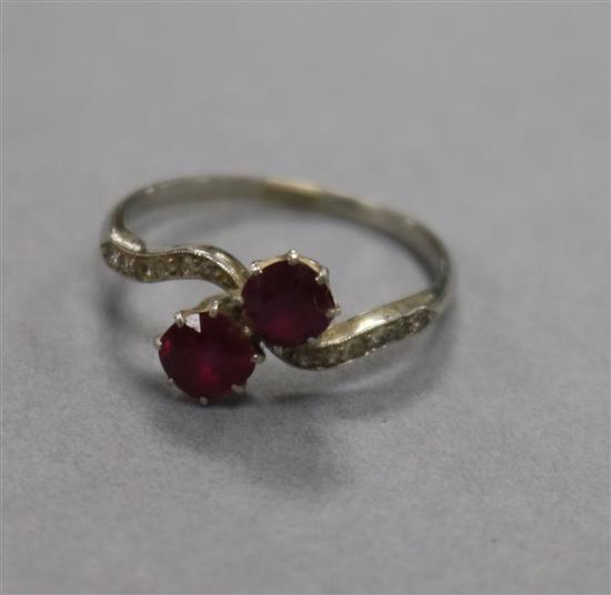 An early 20th century white metal, two stone ruby crossover ring, with diamond set shoulders, size O.